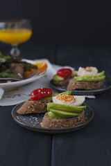 Toasts with avocado, yatsom and cherry tomatoes, on a black wooden background. Juice and delicious food for breakfast. Fitness food. Copy space.