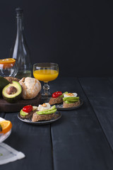 Toasts with avocado, egg and cherry tomatoes, on a black wooden background. Juice and white wine, delicious food for lunch. Copy space.