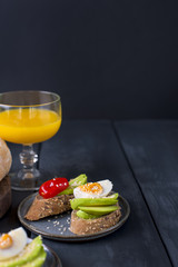 Toasts with avocado, yatsom and cherry tomatoes, on a black wooden background. Juice and delicious food for breakfast. Fitness food.