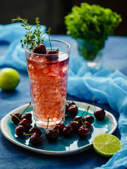  Iced fizzy organic cherry lemonade with fresh berries and thyme on the blue table.