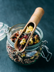 Herbal and fruit teas in glass jars on a dark background. Medicinal herbs. A natural, eco product.Wooden spatula tea spoon.