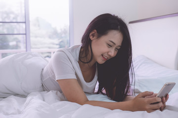 Happy casual young beautiful woman enjoy working on smartphone sitting on the bed in the house.Lazy morning in bed. Relaxing concept