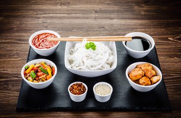 Roasted meat, rice noodles and vegetables on wooden background