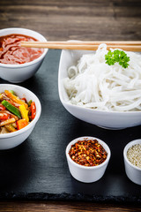Rice noodles and vegetables on wooden background