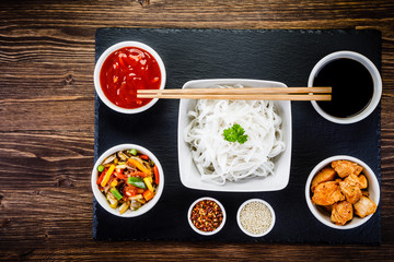 Roasted meat, rice noodles and vegetables on wooden background