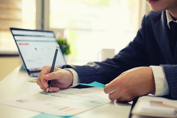 Businessman working with laptop computer analysis data financial in paper and system computer on office table and morning light.