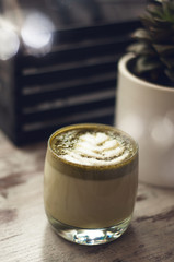 Cup of hot matcha green tea latte with plant on table. Top view of green tea milk. Cappuccino latte art in glass. Flat lay style.