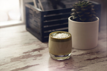 Cup of hot matcha green tea latte with plant on table. Top view of green tea milk. Cappuccino latte art in glass. Flat lay style.