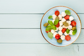 Naklejka na ściany i meble Delicious caprese salad with ripe cherry tomatoes and mini mozzarella cheese balls with fresh basil leaves.