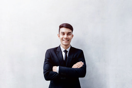 Portrait of Happy Young Businessman standing at the Wall, Smiling and Crossed Arms, Looking at camera