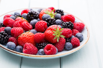 Fresh berry salad on blue dishes. Vintage wooden background.