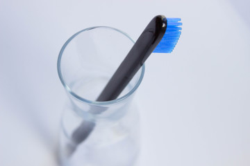 Black style toothbrushes  wiht blue bristle in glass on table on lwhite moning background