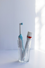 electric toothbrush and toothpaste in a clear glass glass Cup in the morning light on a white background