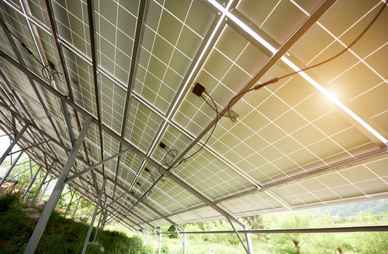 Interior of stand-alone photo voltaic solar system secured on metal rear legs on green grass, lit by summer sun. Alternative energy, environment protection and cheap electricity production concept.