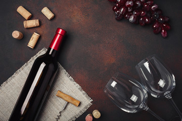 Bottle of wine, two glasses, corkscrew and corks, on rusty background top view
