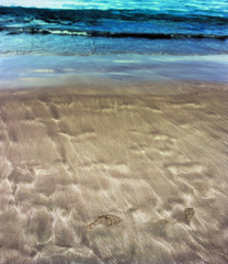 Beautiful patterns from the waves on the sand. Volcanic sand on the beach.  Footprints on sand. Summer
