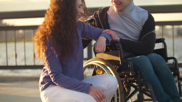 Happy couple - disabled man in wheelchair talking with attractive young woman enjoing the sunset