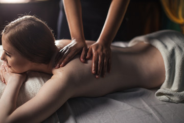 Cropped view of masseuse hands performing shoulder massage on female back