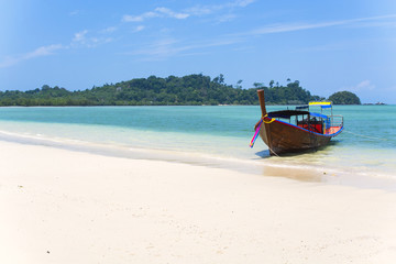 Fototapeta na wymiar Wooden boat on a white sand beach, blue sea with islands in background, tropical beach in Thailand