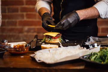 Chef in sterile gloves making beef burgers indoors at the pub kitchen. Street food ready to serve...