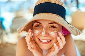 Skincare. Beauty Concept. Young pretty woman applying sun cream  and touch own face. Female in hat...