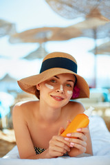 Skincare. Beauty Concept. Young pretty woman holding  sun cream and applying on her face. Female in hat smear  sunscreen lotion on skin and touch own face. Skin Protection and dermatology.