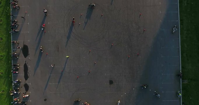 Camera flying up above riding motorcyclists, top view at free skill train on city asphalt square at summer season