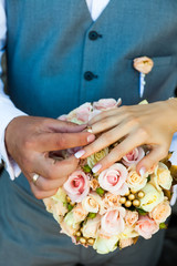 Close-up of hands. The groom dresses the bride's engagement ring on her finger, against the background of a colorful bouquet.