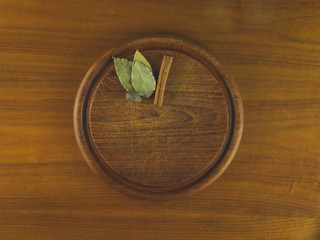 Round wooden cutting board with nutmeg, cinnamon, and bay leaves resting on a wooden table