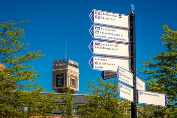 Looking at some route signs at the central train station of Almelo. To the right one of two towers of the former Almelo steam mill is visible. It is now transformed to a business- and health center.