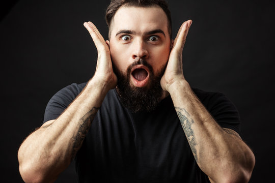 Portrait of athletic rocker and surprised man gesturing in shock and disbelief overacting in shocked hands gesture on isolated black background. Emotion and face expression concept.