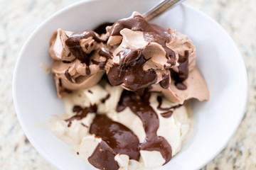 Soft serve vanilla and chocolate ice cream with dark brown syrup drizzled sauce closeup in white bowl with spoon