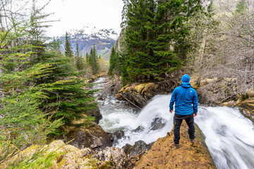 Hiker standing at a waterfall in forest above Geiranger village in Norway