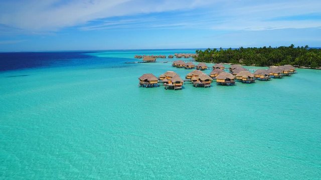 Aerial view of Motu Tautau, palm trees on little islets and turquoise water of blue lagoon, over water bungalows, tropical paradise of South Pacific Ocean - Tahaa island, seascape of French Polynesia