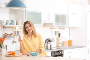 Obraz na płótnie Canvas Beautiful young woman having breakfast and drinking milk in kitchen