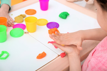 Cute little girl using play dough at table, closeup