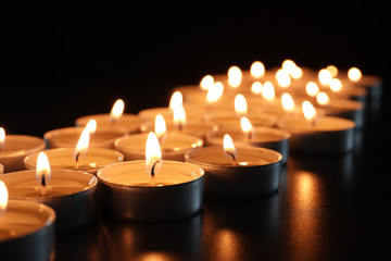 Wax candles burning on table in darkness, closeup