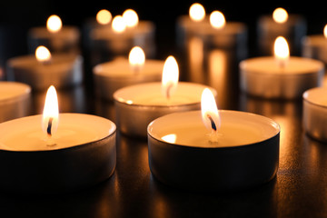 Obraz na płótnie Canvas Wax candles burning on table in darkness, closeup