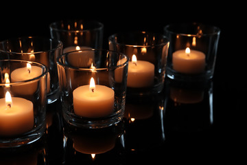 Wax candles burning on table in darkness, closeup