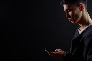 Profile of serious concetrated man using smartphone on dark background with a lot of copyspace.