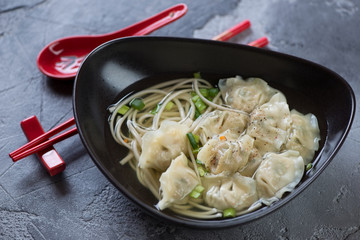 Wonton noodle soup served in a black bowl, selective focus, horizontal shot