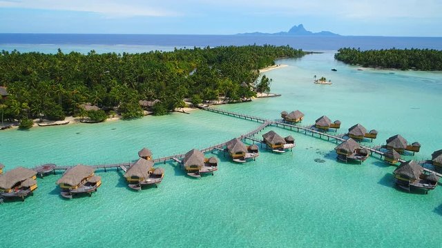 Aerial view of Motu Tautau, palm trees on little islets and turquoise water of blue lagoon, over water bungalows, tropical paradise of South Pacific Ocean - Tahaa island, seascape of French Polynesia