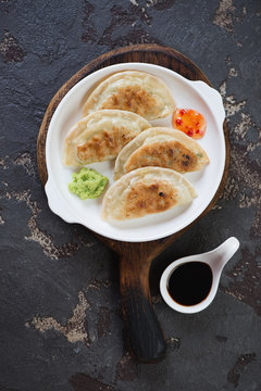 White plate with fried potstickers on a rustic wooden serving board, vertical shot on a brown stone background, top view