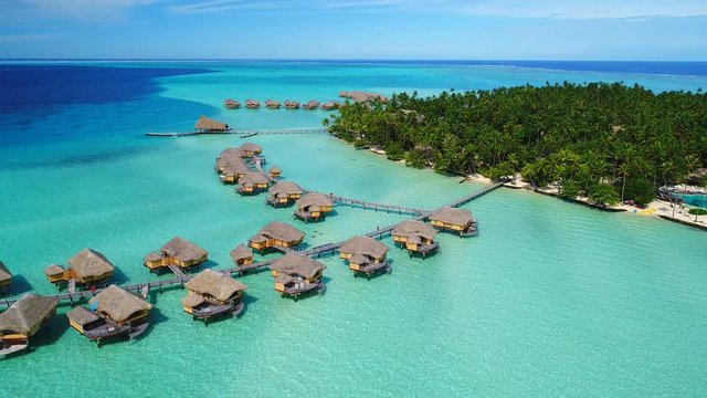 Aerial view of Motu Tautau, palm trees on little islets and turquoise water of blue lagoon, over water bungalows, tropical paradise of South Pacific Ocean - Tahaa island, seascape of French Polynesia