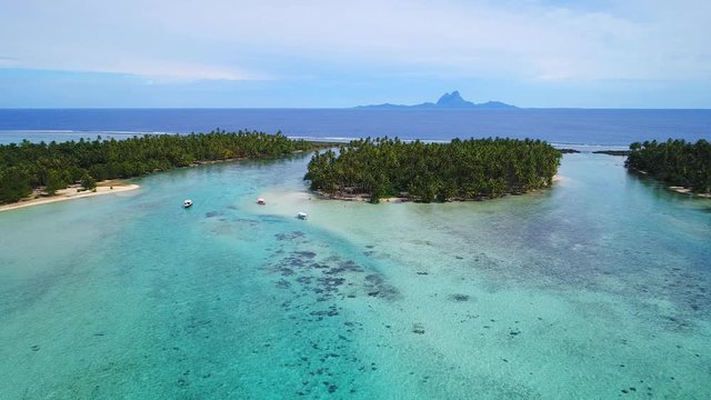 Aerial view of Motu Tautau, palm trees on little islets and clear blue lagoon, coral reef and Bora Bora on background, tropical paradise of Pacific Ocean - Tahaa island, landscape of French Polynesia