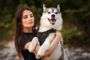 Naklejka na ściany i meble Beautiful girl plays with a dog, grey and white husky, in the mountains at sunset.