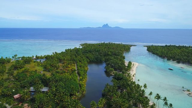 Aerial view of Motu Tautau, palm trees on little islets and clear blue lagoon, coral reef and Bora Bora on background, tropical paradise of Pacific Ocean - Tahaa island, landscape of French Polynesia