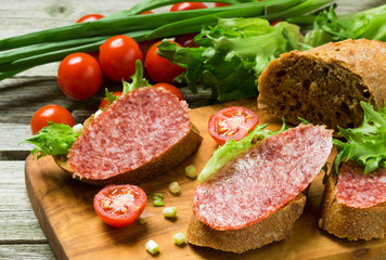Sandwiches with sausage, tomatoes, onions on a cutting board.
