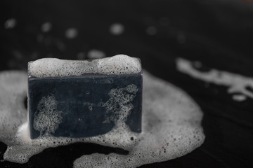 block of natural carbon charcoal soap on black stone background with bubbles - 207536933