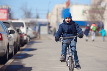 Joyful Caucasian boy riding a bicycle in a city street.